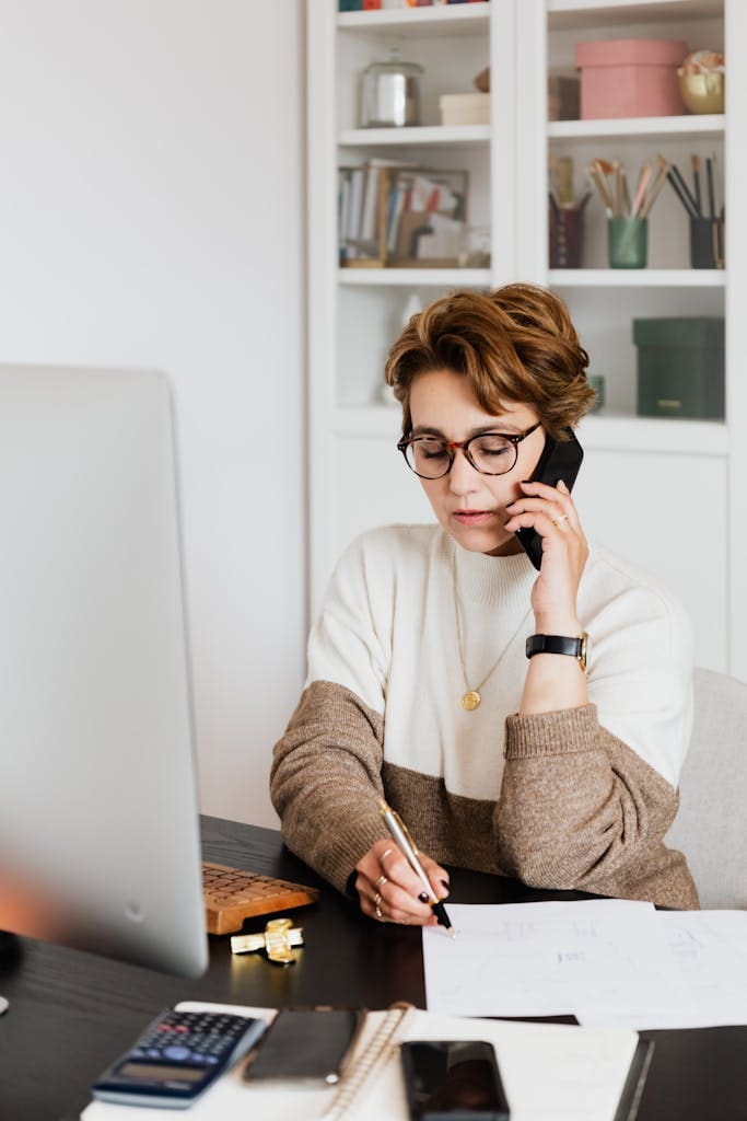 Professional woman multitasking in her workspace with phone and laptop.